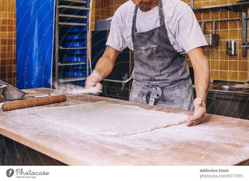 Kropfenkoch bestreut den Teig mit Mehl bestäuben Teigwaren Bäcker Mann Koch Prozess vorbereiten roh Streuung männlich Bäckerei dreckig Schürze Tisch