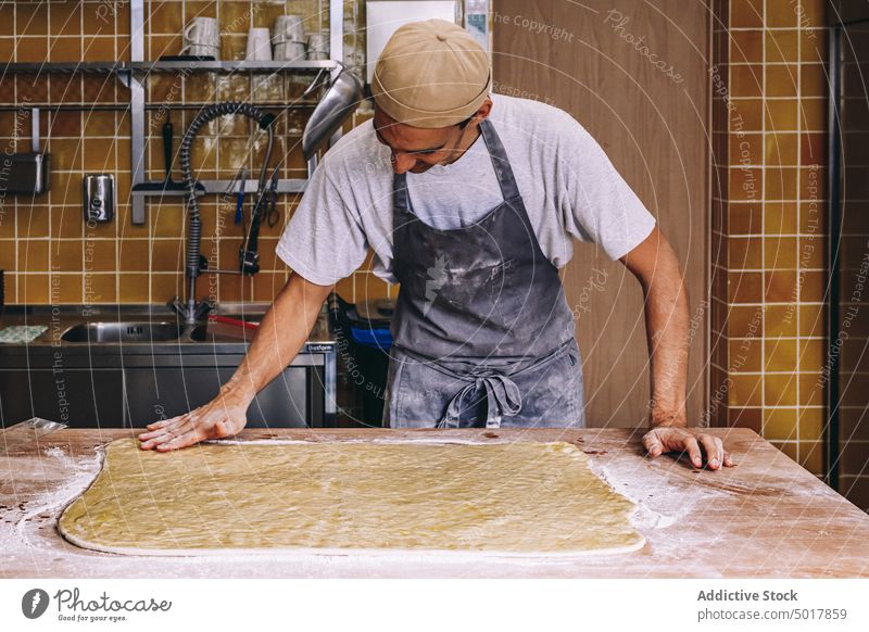 Koch bereitet Teig zum Backen vor Teigwaren Bäcker Mann roh Prozess vorbereiten Mehl männlich Bäckerei dreckig Schürze Tisch Lebensmittel Arbeit Rezept Job