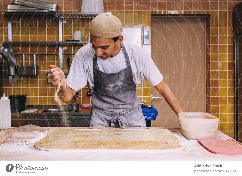 Koch bestreut den Teig mit Mehl bestäuben Teigwaren Bäcker Mann Prozess vorbereiten roh Streuung männlich Bäckerei dreckig Schürze Tisch Lebensmittel Arbeit