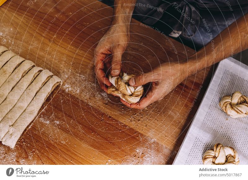 Anonymer männlicher Bäcker beim Backen von Zimtschnecken Teigwaren vorbereiten Mann rollen Brötchen roh ungekocht Form Prozess Koch Bäckerei Mehl Tisch hölzern