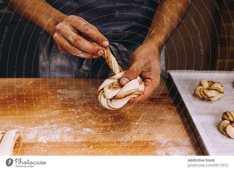 Männlicher Bäcker beim Backen von Zimtschnecken Teigwaren vorbereiten Mann rollen Brötchen roh ungekocht Form Prozess männlich Koch Bäckerei Mehl Tisch hölzern