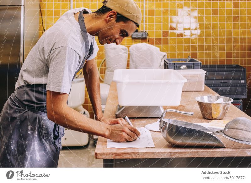 Bäcker macht sich während der Teigzubereitung Notizen Bäckerei Mann Arbeit zur Kenntnis nehmen schreiben vorbereiten Skala Gewicht professionell Küche männlich