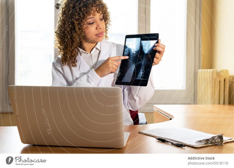 Crop ethnischen Arzt zeigt Röntgenbild gegen Laptop im Büro Sanitäter Bild Stachel Diagnostik analysieren professionell Frau Punkt Röntgenaufnahme Analyse