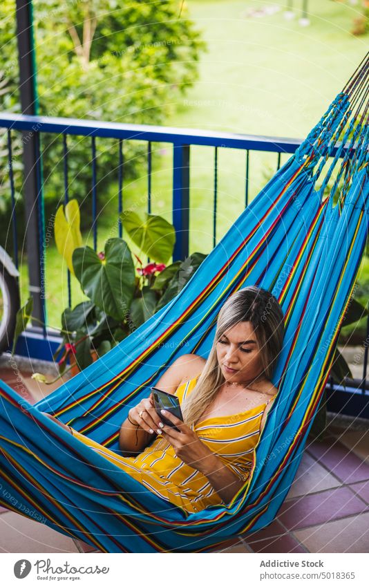 Frau surft auf dem Smartphone und ruht sich in der Hängematte aus benutzend Kälte Terrasse Resort sich[Akk] entspannen Veranda Browsen Mobile Sommer ruhen