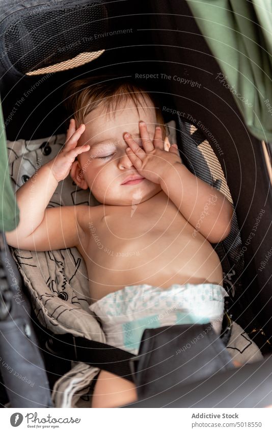 Kleinkind im Kinderwagen liegend mit Händen im Gesicht Baby Lügen schlafen Hand im Gesicht bezaubernd ohne Hemd ruhen unschuldig Kindheit Säuglingsalter Windel