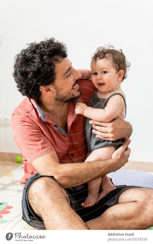 Fröhlicher junger Vater mit Baby, das auf einer Matte sitzend mit Spielzeug spielt Mann spielen Glück aufgeregt Zusammensein schließen Liebe heiter Freude