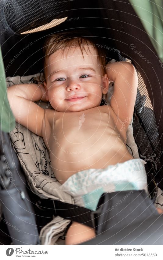 Lustiges Kleinkind im Kinderwagen liegend mit Händen hinter dem Kopf Baby Lügen Lächeln Glück Hand hinter dem Kopf bezaubernd ohne Hemd Freude ruhen niedlich