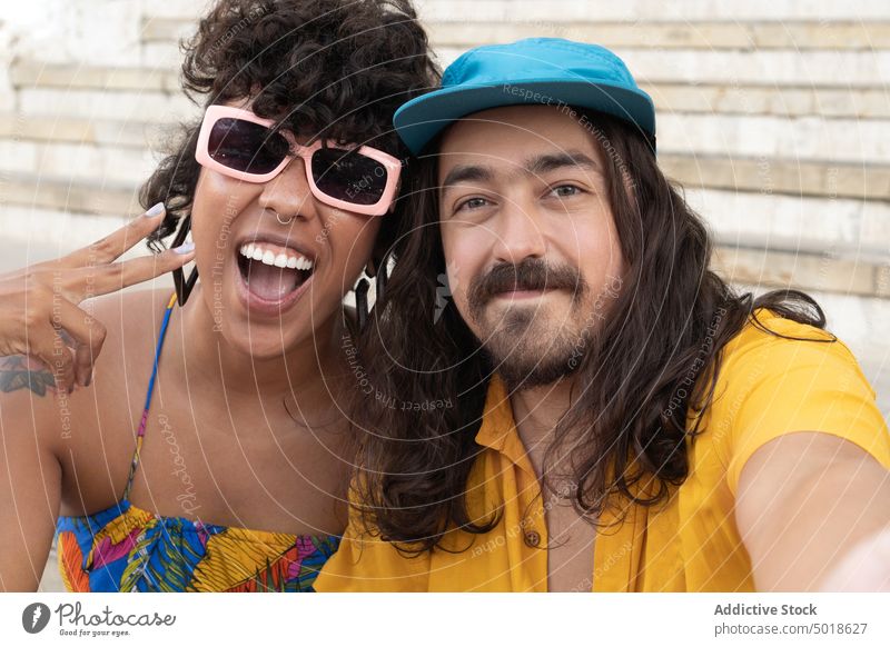 Cooles ethnisches Paar, das sich umarmt und ein Selfie macht Hipster Selbstportrait cool farbenfroh gestikulieren Spaß haben v-Zeichen Umarmen Zusammensein