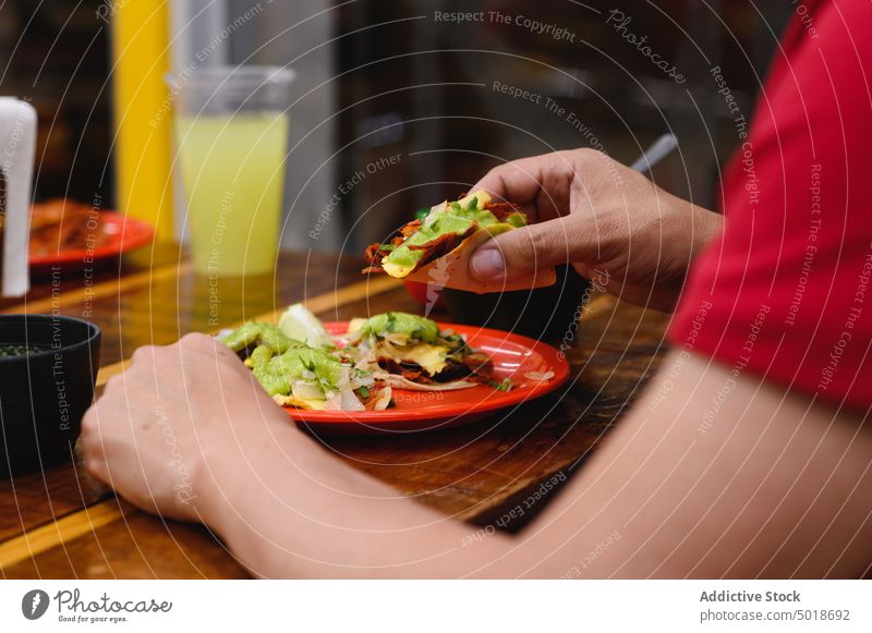 Crop-Person isst leckeren Taco am Tisch Straßenessen mexikanisches Essen Mittagessen Mahlzeit Speise Abendessen Restaurant Tortilla Kultur Tradition Glas
