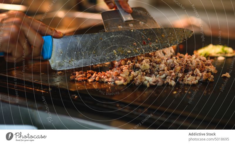 Kropfenkoch beim Schneiden von Fleischscheiben auf der Grillplatte bei der Arbeit Küchenchef Schweinefleisch hacken Messer Spachtel Bratpfanne Beruf Restaurant