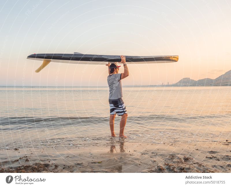 Mann hält Surfbrett über den Kopf und schaut entlang Seeküste Sommer Urlaub Wasser Strand Sport MEER Meer Surfer Lifestyle Freizeit Erholung aktiv Sand Hobby
