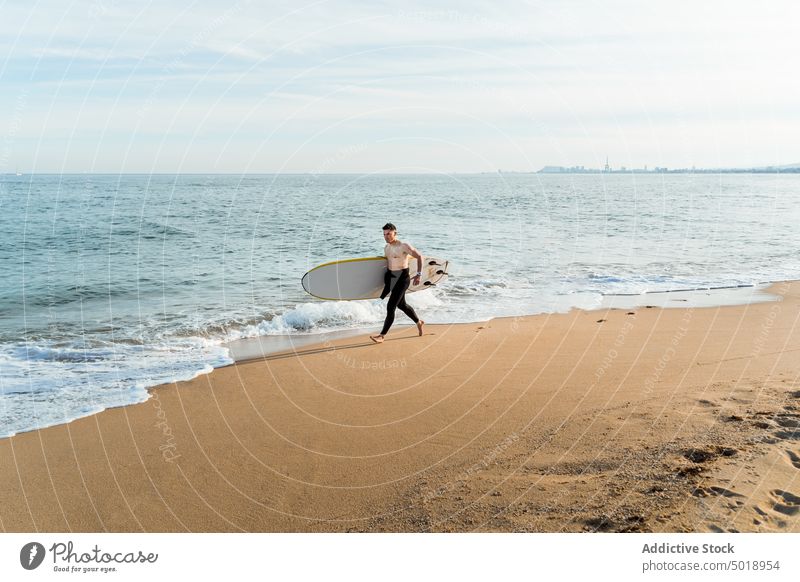 Junger Mann mit Surfbrett am Strand Surfer MEER winken aktiv sportlich Sommer Meer ohne Hemd männlich jung Sport Ufer Meeresufer Aktivität Sand Urlaub Athlet