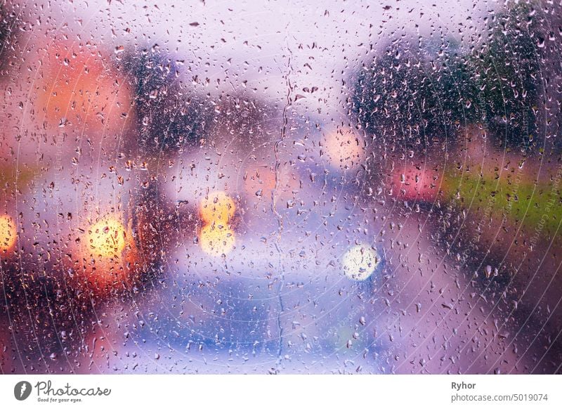 Wassertropfen von Regen auf blauem Glas Hintergrund. Straße Bokeh Lichter aus dem Fokus. Herbst Abstrakte Kulisse pulsierend farbenfroh glühen fallen abstrakt