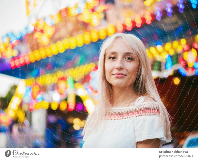 Junges attraktives blondes Mädchen, das in der Nähe eines Karussells im Vergnügungspark steht. Schönes Porträt einer Frau mit langen Haaren. Erwachsener