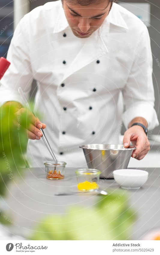 Profikoch benutzt beim Kochen eine Pinzette Küchenchef Essen zubereiten professionell benutzend Mann vorbereitend Speise Restaurant fokussiert ausgefallen ernst