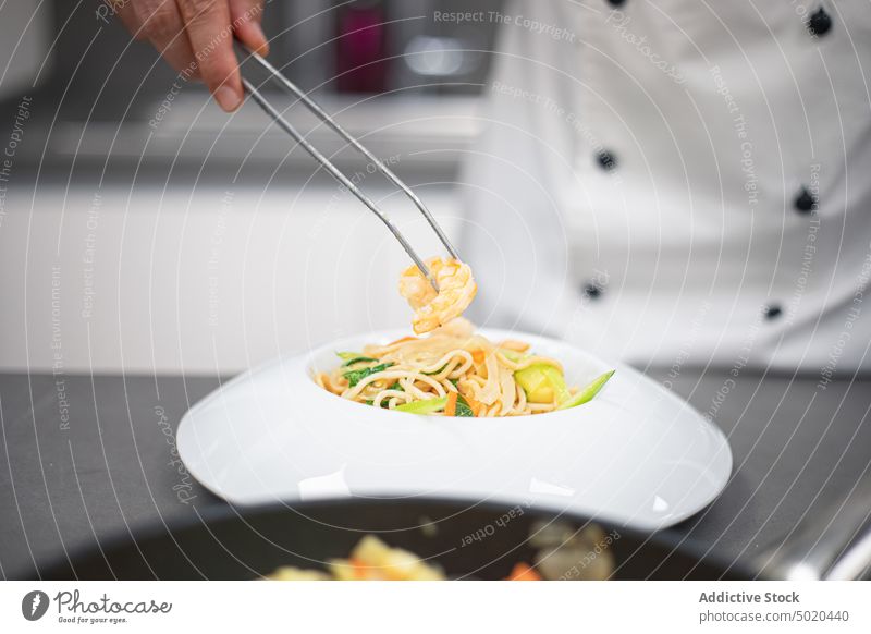 Professioneller Koch benutzt eine Pinzette, um ein Gericht in einem schicken Teller zu servieren Küchenchef Servieren professionell benutzend Mann vorbereitend