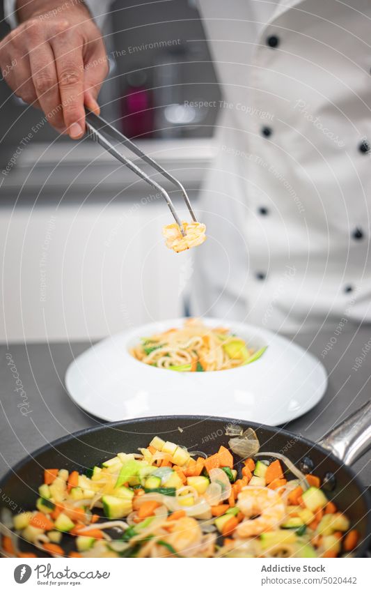 Professioneller Koch benutzt eine Pinzette, um ein Gericht in einem schicken Teller zu servieren Küchenchef Servieren professionell benutzend Mann vorbereitend
