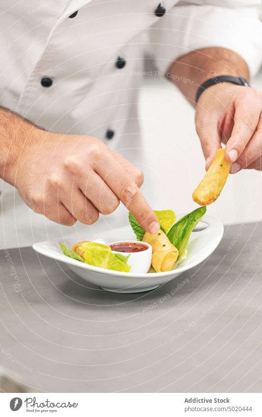 Profikoch serviert Frühlingsrollen auf einem Teller Küchenchef Servieren professionell Speise Küchenkräuter ausgefallen Saucen Restaurant Tisch Mann weiß