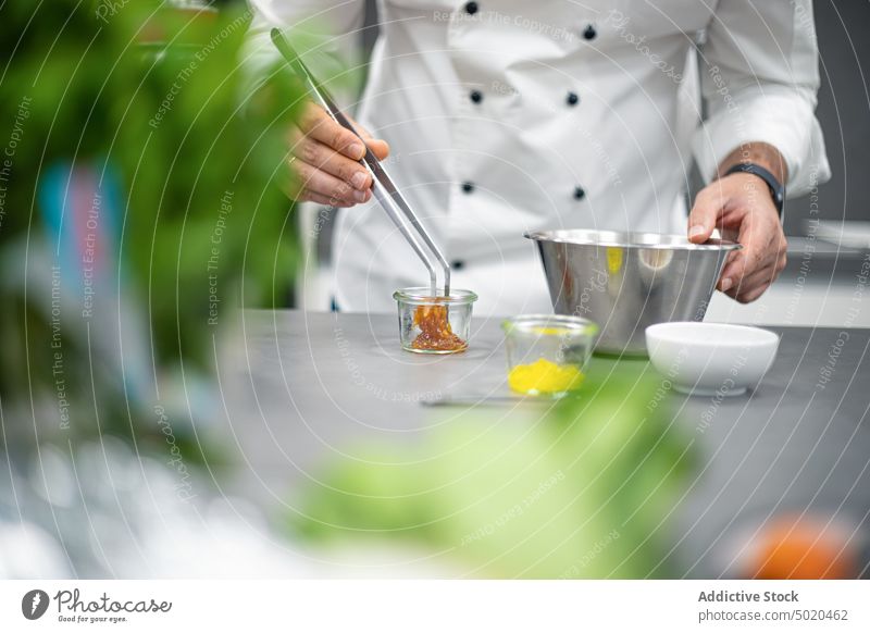 Unbekannter Koch, der mit einer Zange in der Nähe von Zutaten in Gläsern Essen zubereitet Mann Küchenchef Bestandteil Tisch Prozess mischen Glas männlich