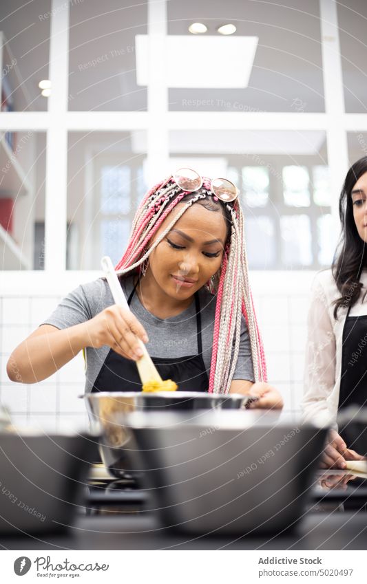 Inhalt Multiethnische Frauen rühren bei einem Kochworkshop ein Gericht im Topf um Essen zubereiten Werkstatt Lächeln rostfrei Speise Kochen lässig stehen