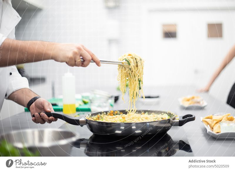 Crop-Mann in weißer Kochjacke fängt Spaghetti aus der Pfanne Küchenchef demonstrierend Speise Servieren Essen zubereiten Werkstatt professionell Restaurant