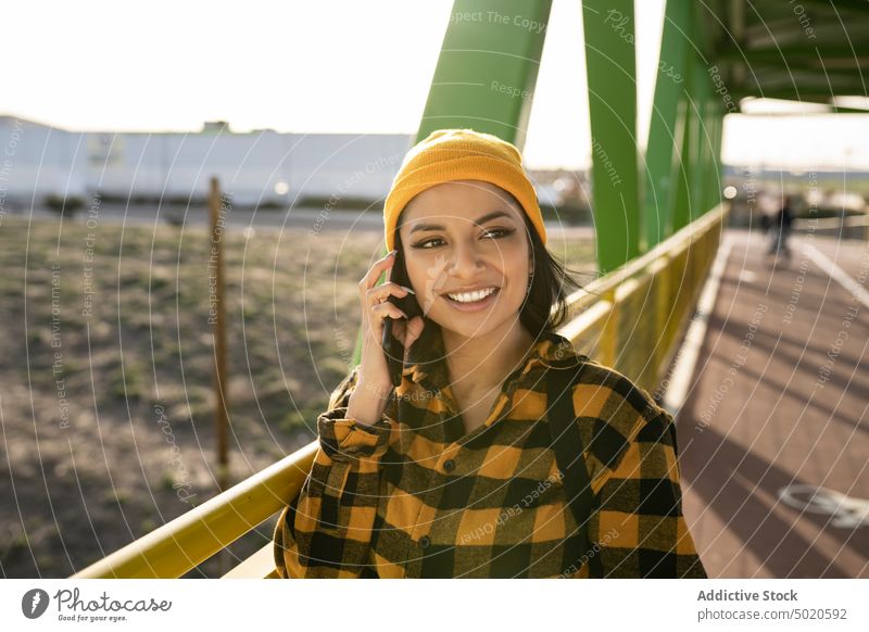 Lächelnde junge ethnische Frau, die auf einer Brücke mit ihrem Smartphone spricht sprechend Stil Inhalt SMS positiv benutzend Mobile Telefon Lateinamerikaner