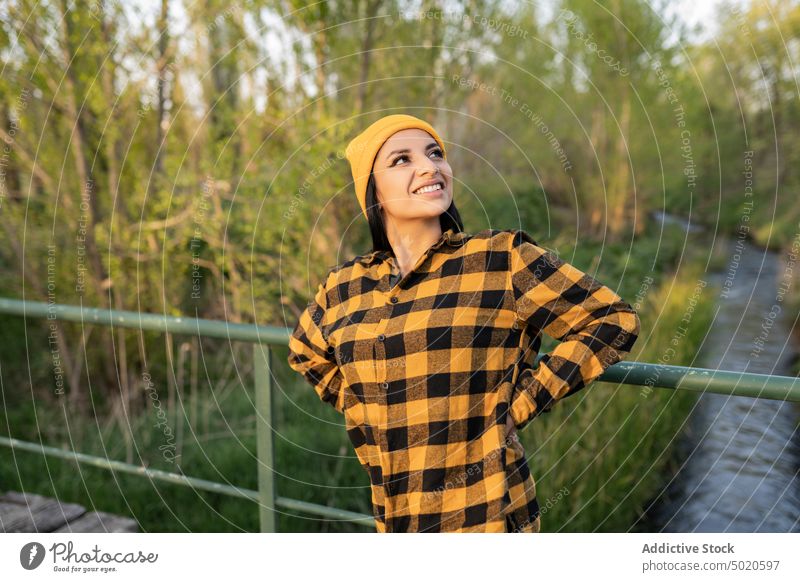 Selbstbewusste junge ethnische Wanderin steht auf einer Holzbrücke über einen Fluss in der Natur Frau Lächeln Wanderer Glück Inhalt Steg genießen reisen Brücke