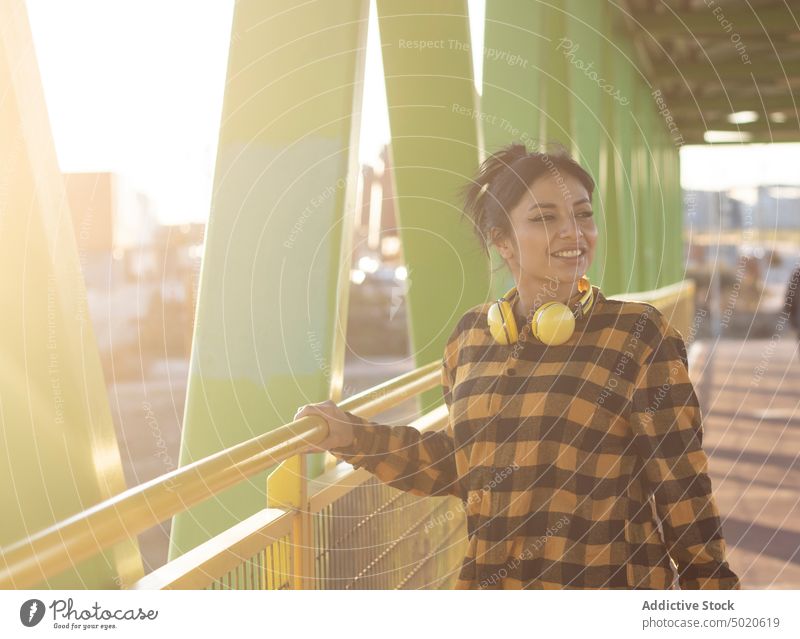 Glückliche junge lateinamerikanische Frau lächelt, während sie auf einer Brücke in der Stadt steht Lächeln Stil Spazierweg Optimist positiv Sonnenlicht genießen