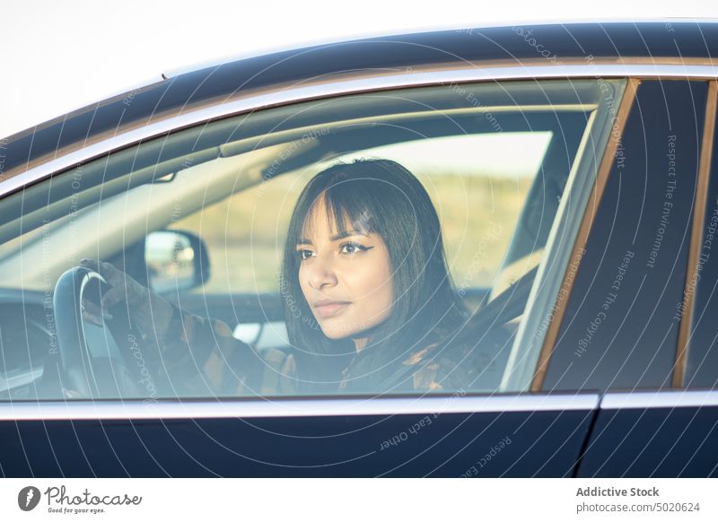 Aufmerksame junge ethnische Frau fährt Auto auf dem Lande Laufwerk PKW achtsam Fahrzeug Fahrer Landschaft Straße Autoreise Verkehr Windstille Stil