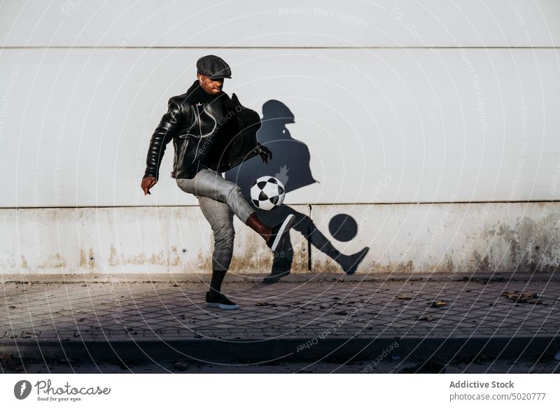 Schwarzer Mann kickt Ball auf der Straße tretend schwarz Afrikanisch Amerikaner springend Wand schäbig Fußball Spiel Aktivität männlich Straßenbelag Bürgersteig