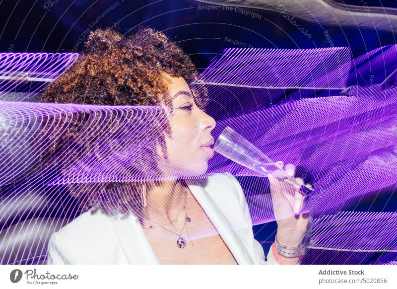 Ethnische Frau trinkt Champagner während einer Party Nachtleben trinken ethnisch Nachtclub neonfarbig leuchten Stil violettes Licht Reflexion & Spiegelung