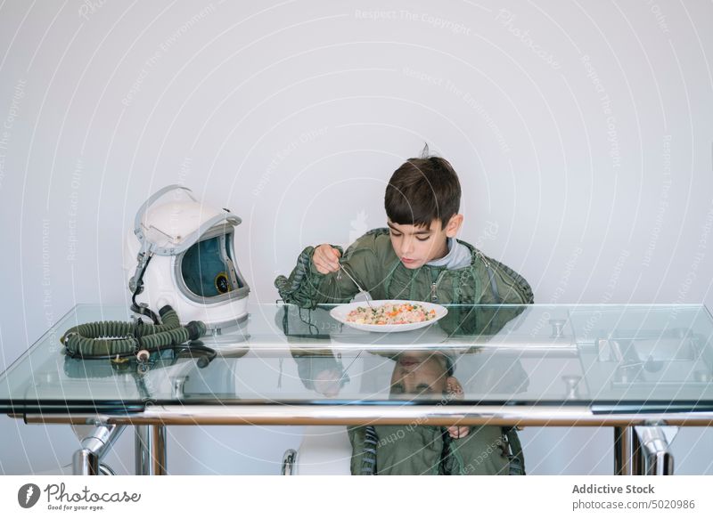 Junge im Astronautenkostüm sitzt am Tisch und isst Hintergrund Kind Kindheit Konzept Tracht Schaffung handgefertigt Schutzhelm Vorstellungskraft einfallsreich