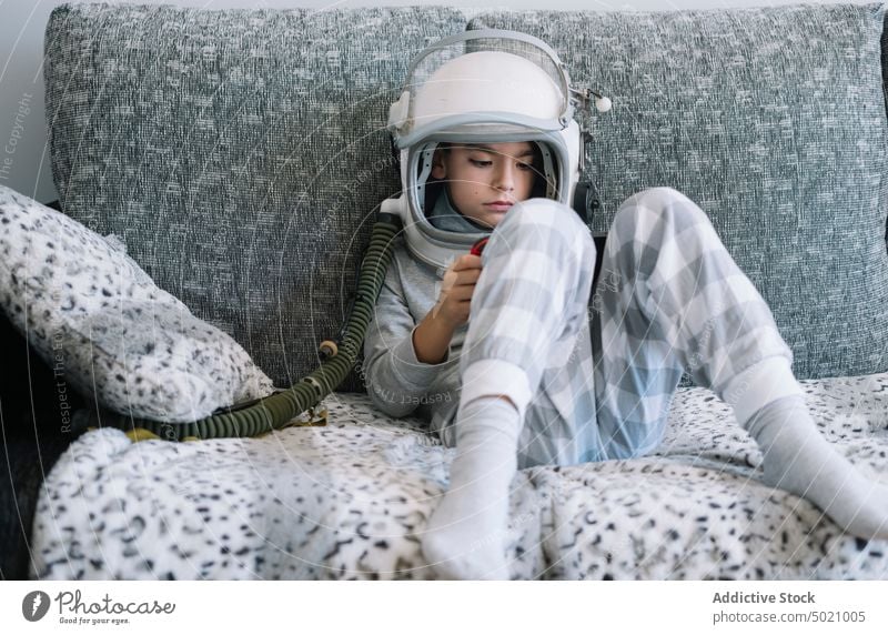 Kind liegt auf der Couch und spielt mit einer Videospielkonsole zu Hause Astronaut Hintergrund Junge Kindheit Konzept Tracht Schaffung handgefertigt Schutzhelm