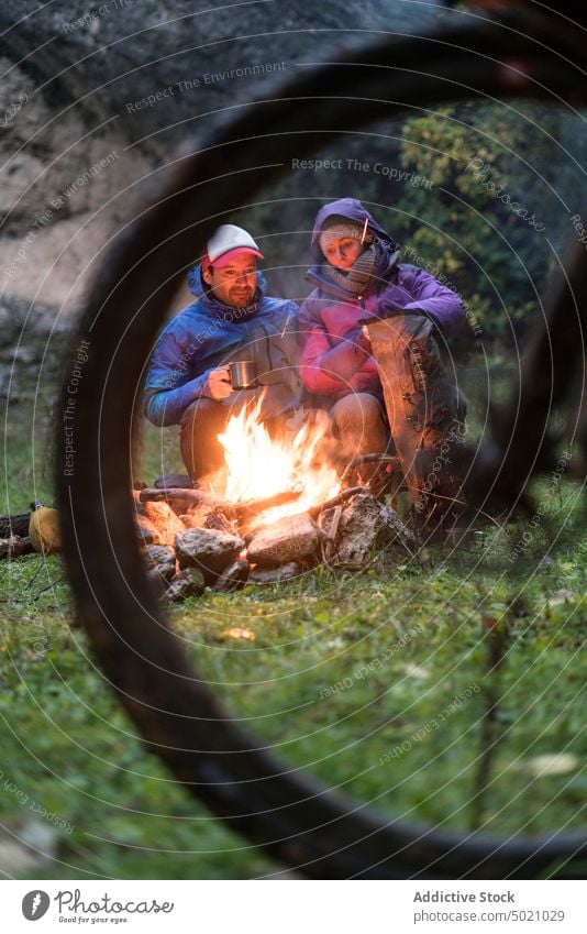 Menschen in warmer Kleidung sitzen am Feuer und trinken ein warmes Getränk aus einem Becher Fahrrad Flamme Abenteuer Zusammensein erwärmen Freundschaft aktiv