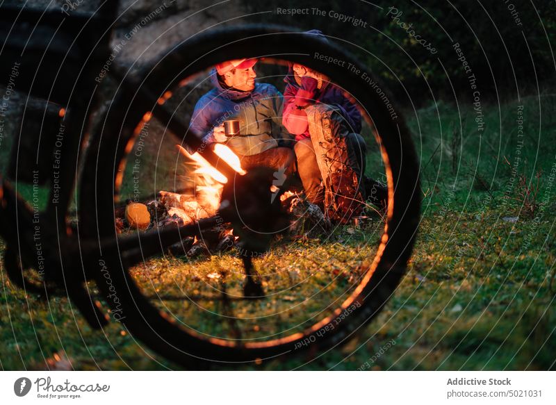 Menschen in warmer Kleidung sitzen am Feuer und trinken ein warmes Getränk aus einem Becher Fahrrad Flamme Abenteuer Zusammensein erwärmen Freundschaft aktiv
