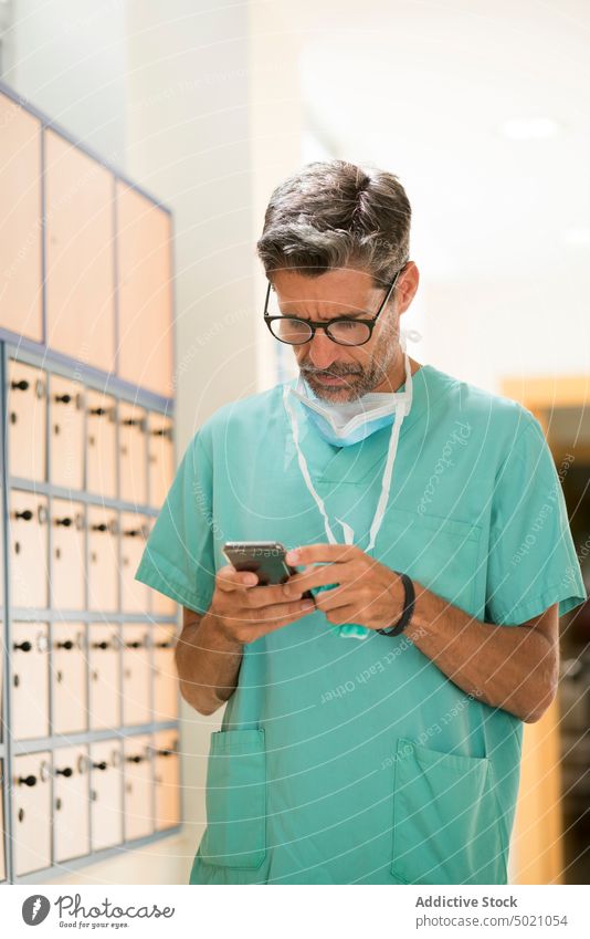 Seriöser Chirurg mit Smartphone Krankenhaus benutzend ernst Gang Mann Erwachsener Arzt Medizin Gesundheitswesen Pause Uniform Technik & Technologie Gerät