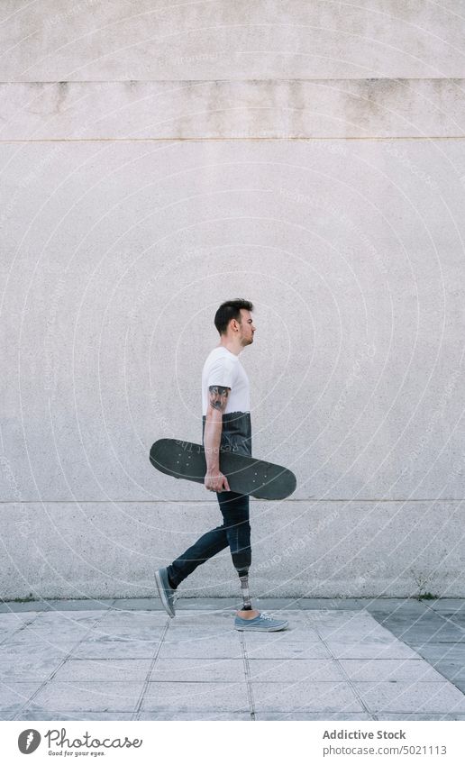 Mann mit Beinprothese geht mit Skateboard in der Hand Mitfahrgelegenheit künstlich Tatkraft Motivation dynamisch Wand Straße Amputierte Großstadt Außenseite