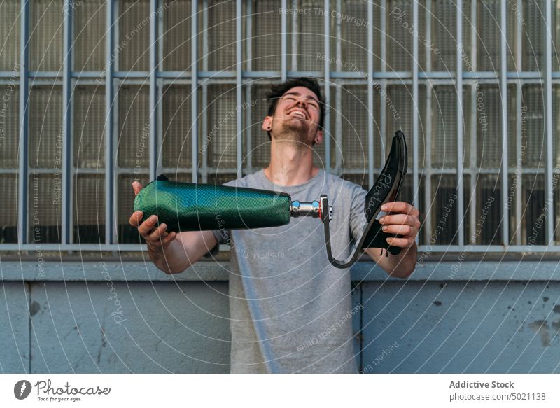 Fröhlicher Mann zeigt Beinprothese künstlich zeigend Straße Großstadt Akzeptanz stark Lächeln Lachen deaktiviert urban Gebäude Wand männlich Herausforderung