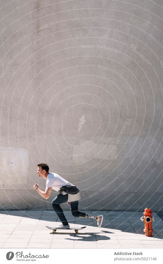 Mann mit Beinprothese fährt Skateboard Mitfahrgelegenheit künstlich Tatkraft Motivation dynamisch Wand Straße Amputierte Großstadt Außenseite jung Beton Energie
