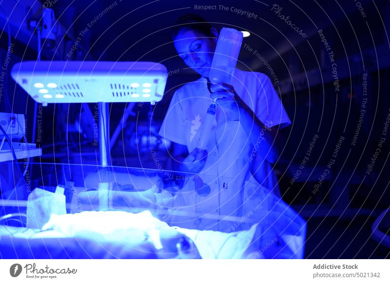 Weiblicher Arzt nimmt Medizin aus der Flasche neonatal Krankenhaus Station Arbeit Spritze Brutkasten Frau Nacht Illumination blau Umschalttaste Medikament