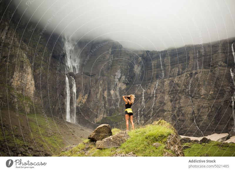 Anonymer weiblicher Reisender in der Nähe einer Klippe mit Wasserfall Frau Berge u. Gebirge Felsen Ausflug bedeckt wolkig Natur Landschaft Pyrenäen