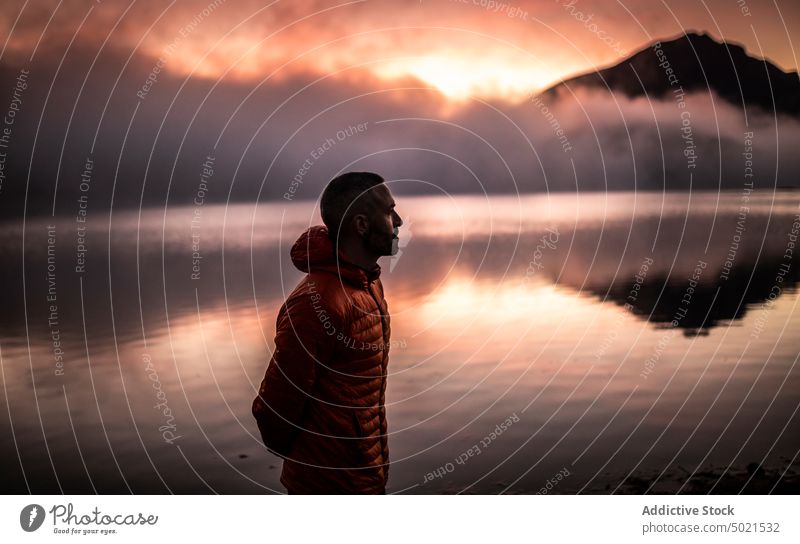 Männlicher Reisender, der den Sonnenuntergang in der Nähe eines Bergsees betrachtet Mann See Berge u. Gebirge allein Natur Reflexion & Spiegelung nachdenken