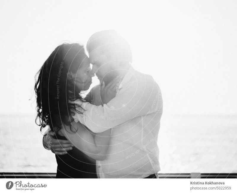 Porträt eines jungen attraktiven Paares, das in der Nähe des Meeres oder Ozeans Latin Bachata tanzt. Sonnenlicht Hintergrund. Mann umarmt sanft sein geliebtes Mädchen und schaut sie mit Bewunderung an