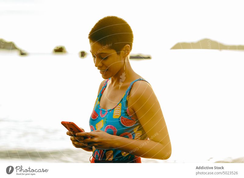 Ethnische Frau, die am Strand auf ihrem Smartphone surft Sommer MEER Telefon Kommunizieren Glück jung ethnisch Lateinamerikaner Mobile Browsen Lächeln