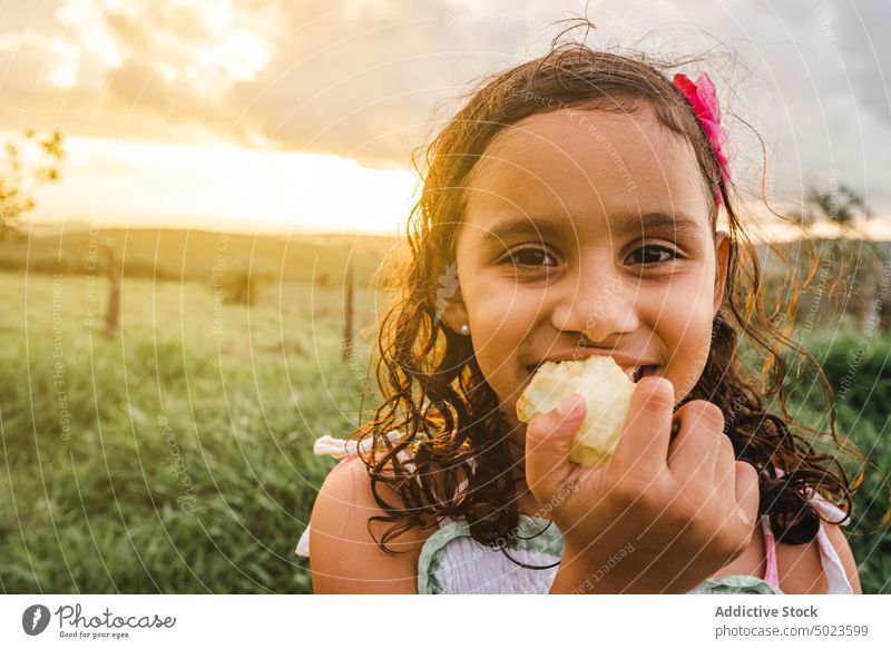 Hispanisches Mädchen isst Apfel auf dem Lande essen Natur ruhen Sonnenuntergang Biss Glück Wochenende Sommer Kind bezaubernd Feld Lächeln niedlich Blume
