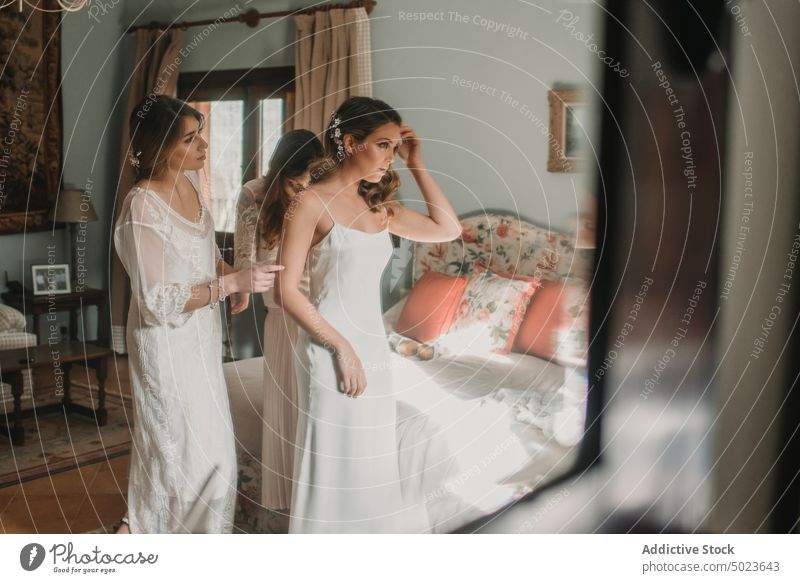 Fröhliche Frauen helfen einer Dame im Schlafzimmer beim Anziehen eines Kleides Hilfe Bekleidung heiter Hochzeit Bett Glück jung attraktiv einsteigend