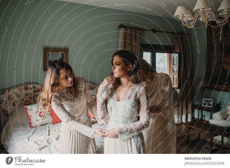 Fröhliche Frauen helfen einer Dame im Schlafzimmer beim Anziehen eines Kleides Hilfe Bekleidung heiter Hochzeit Bett Glück jung attraktiv einsteigend