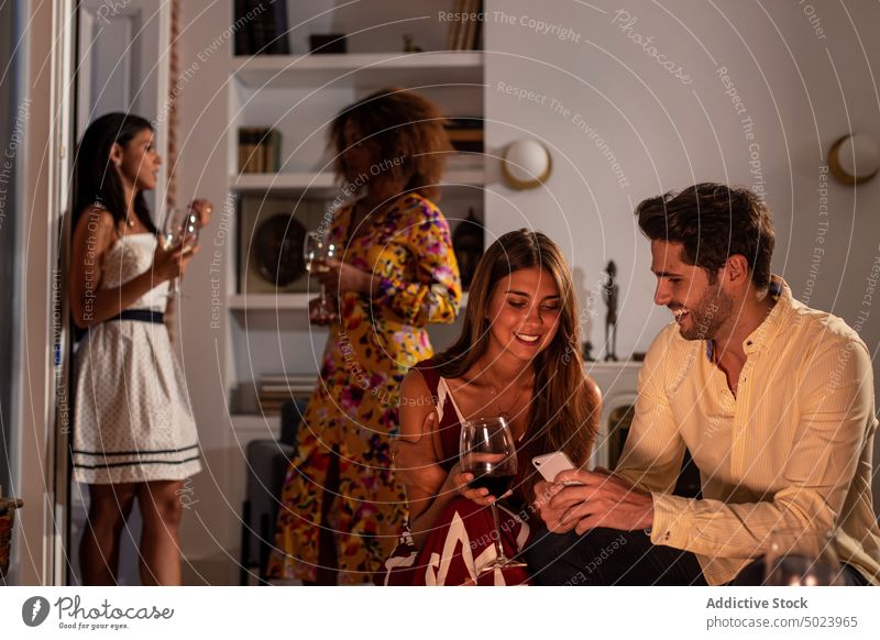 Glückliches Paar mit Smartphone auf Party mit Freund auf dem Hintergrund benutzend teilen Foto Funktelefon ruhen Zusammensein heimwärts Mitteilung Anschluss