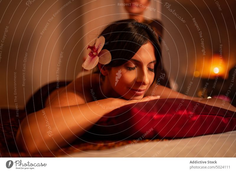 Attraktive Frau auf dem Bett eines Massagesalons liegend Klient Kaukasier geschlossene Augen Orchidee ohne Hemd ruhen Thaimassage Behandlung Therapie asiatisch