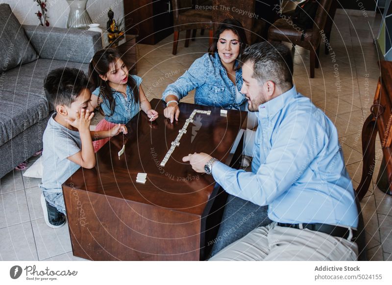 Erfreute ethnische Familie lächelt beim Spielen eines Brettspiels am Wochenende zu Hause Frau Kinder spielen Mann Fliesen u. Kacheln Konzentration Zusammensein